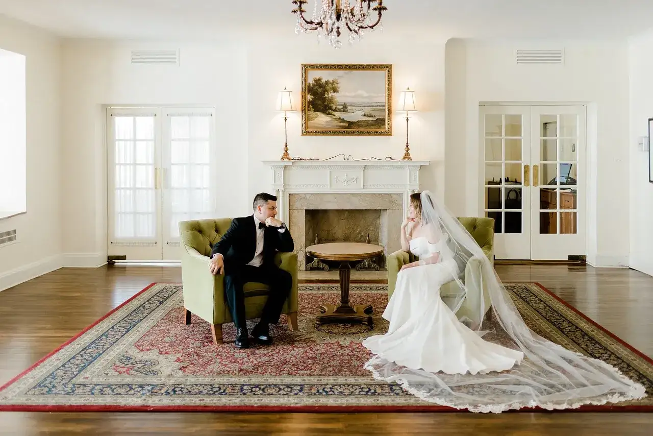 Para młoda po ślubie cywilnym siedzi naprzeciwko siebie w eleganckich fotelach, wpatrując się w siebie z miłością.
