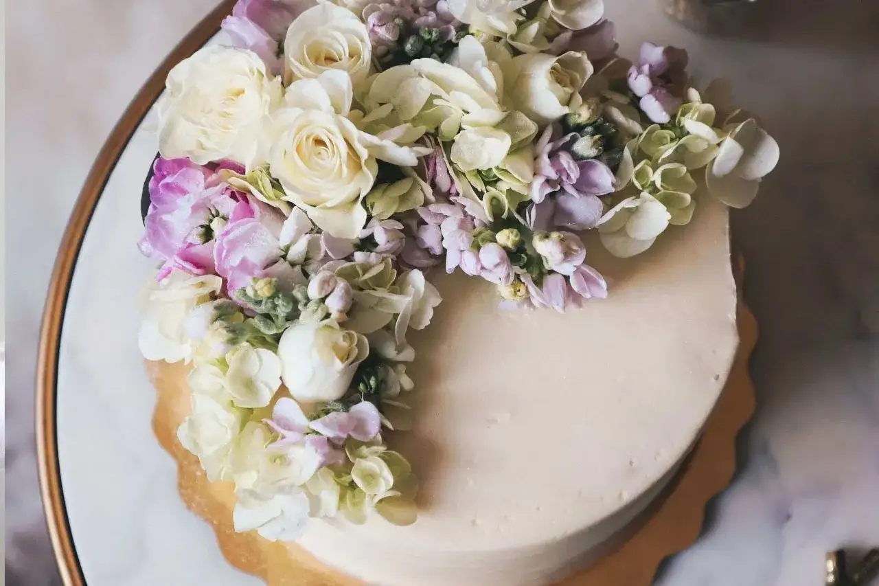 Elegancki tort weselny z żywymi kwiatami w pastelowych kolorach, ozdobiony bukietem róż, hortensji i innych delikatnych kwiatów.