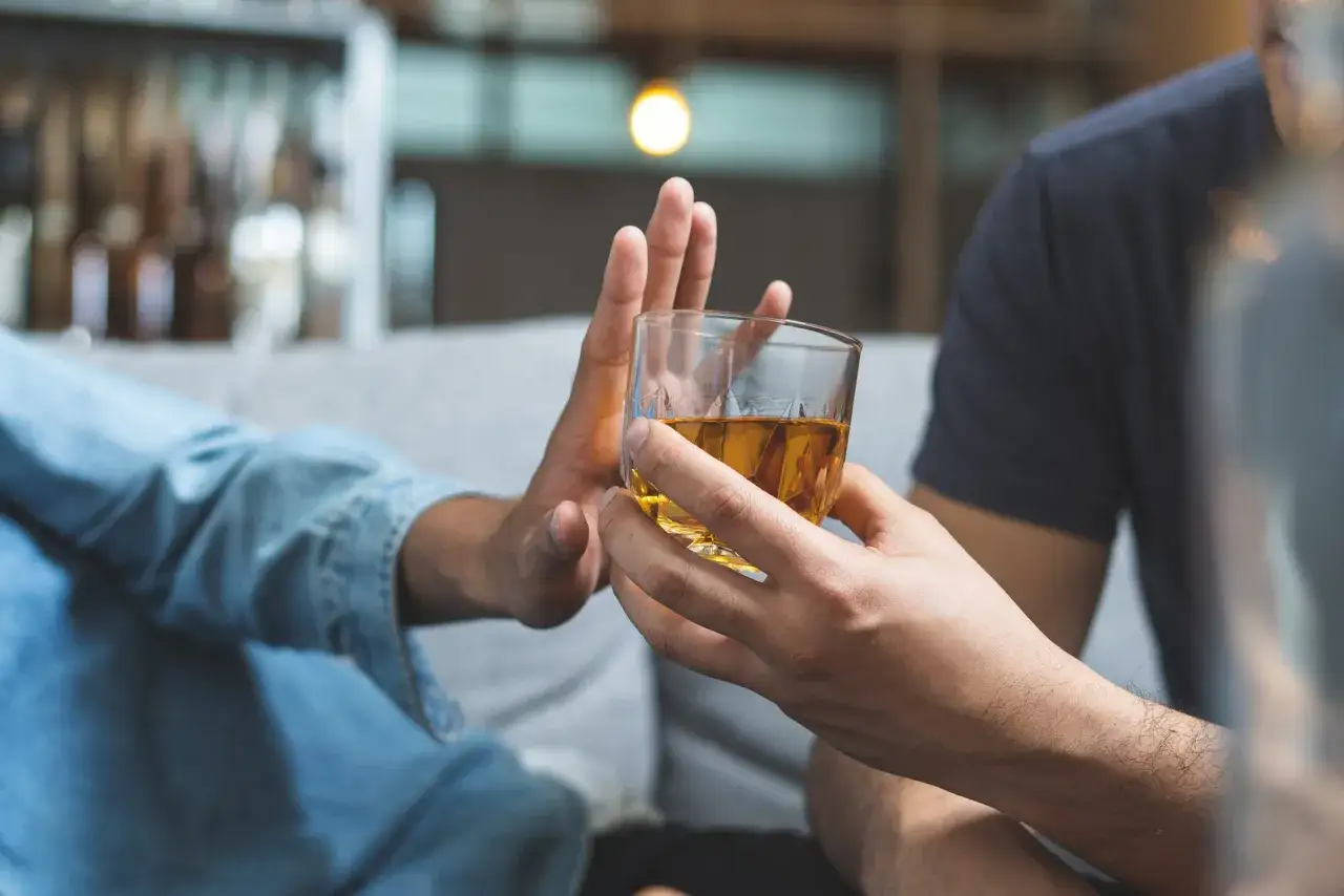 Dłoń odrzuca szklankę z alkoholem. Pokazuje asertywne odmawianie picia alkoholu przykłady.