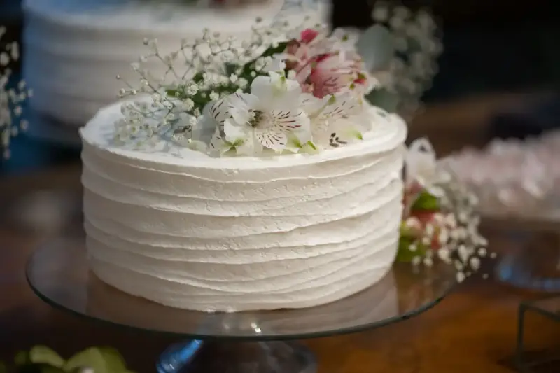 Elegancki tort weselny z żywymi kwiatami, udekorowany delikatnymi białymi kwiatami i gipsówką.